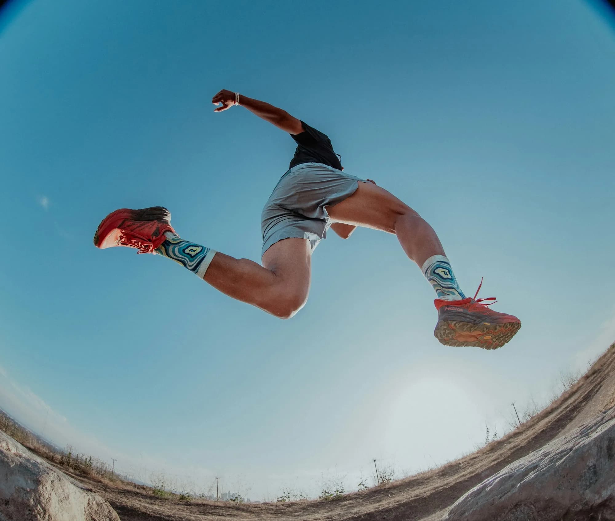 A trail runner leaping mid-stride against a deep blue sky.